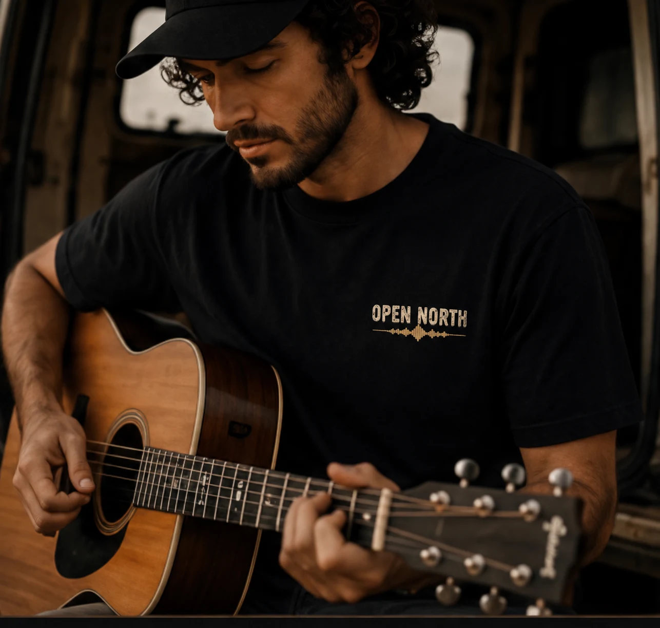 Homem tocando violão vestindo a camiseta Sound preta, com o selo Open North no peito.